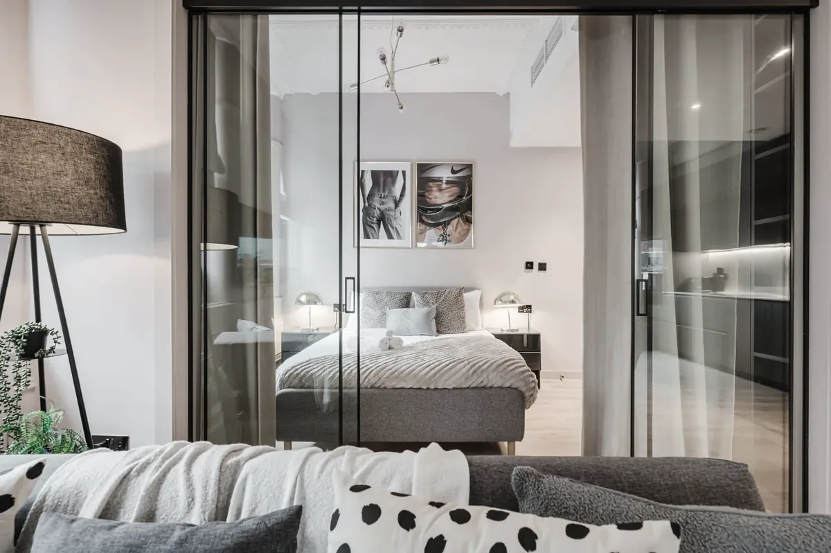 Manchester apartment under Beyond Stays property management. Crittall-style glass partition dividing the styled bedroom from open-plan living.